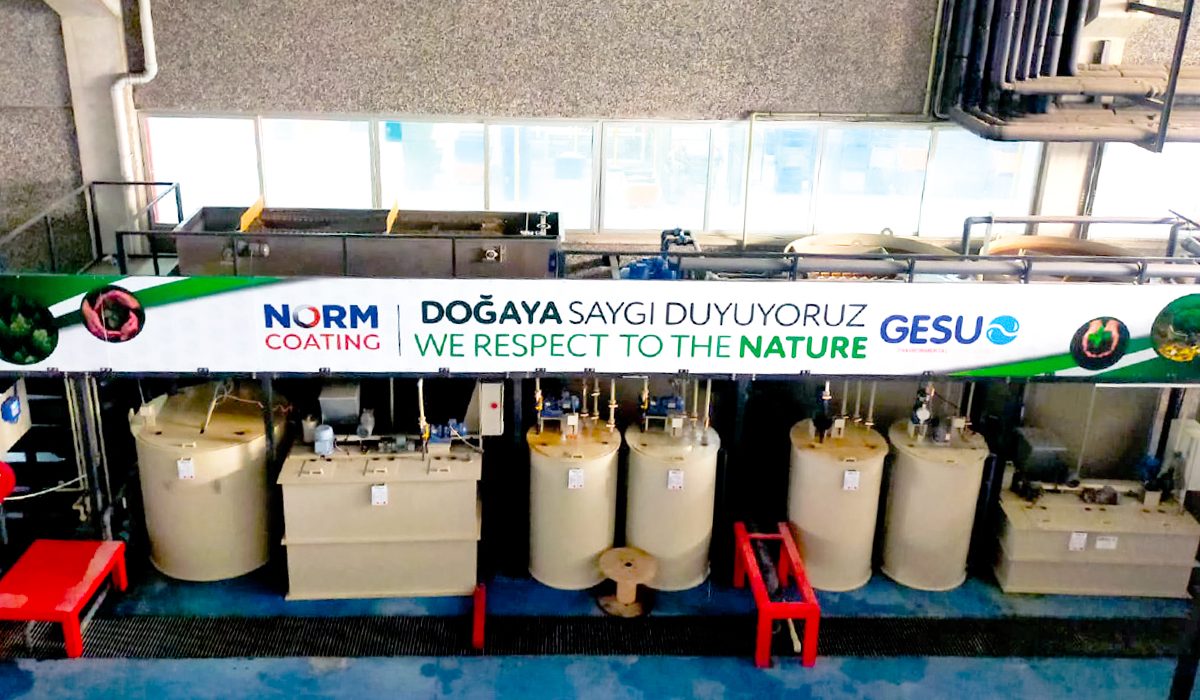 The 'NORM COATING — We Respect Nature — GESU' banner hung by the customer at the Norm Coating plant, with GESU chemical treatment tanks
