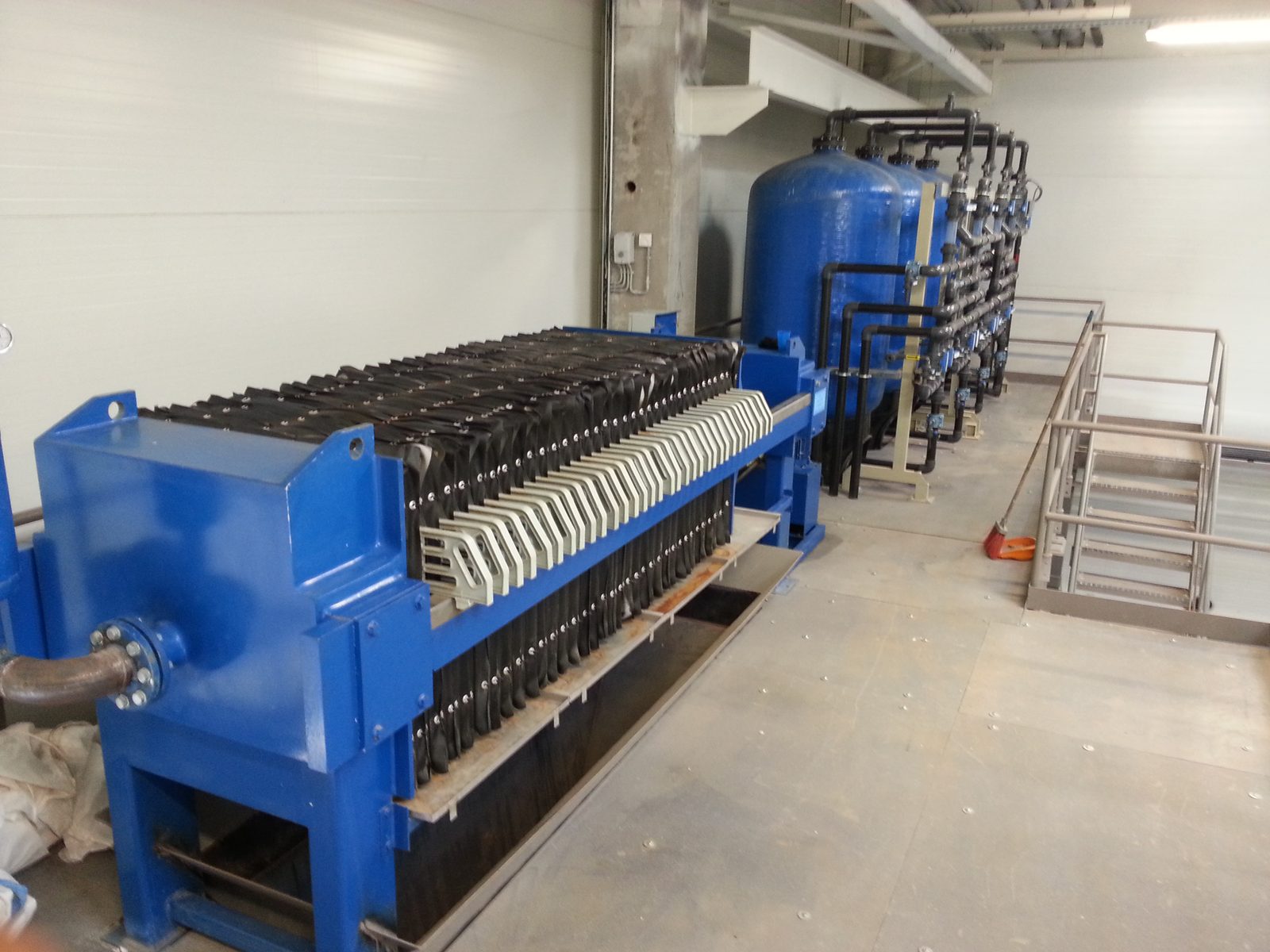 Plate filter press for sludge dewatering; blue pressure-filter group and service platform behind